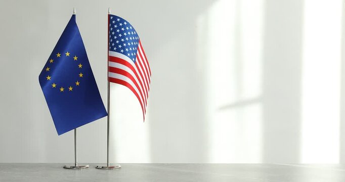 Woman putting flag of European Union next to American on table against light background, closeup