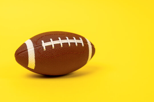 A textured brown American football ball with white laces and stripes rests on a vivid yellow studio backdrop, leaving open copy space for a game day, sports league or Super Bowl party promotion.
