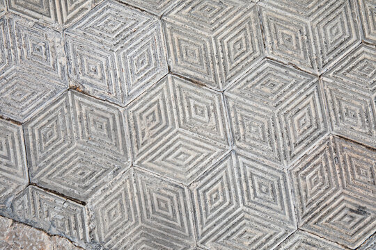 Weathered geometric concrete paving tiles form a repeating three-dimensional sidewalk pattern