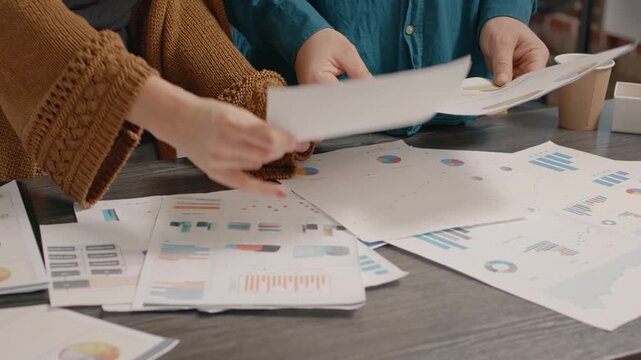 Reports, comparison and planning in a close-up of coworkers lifting and rearranging printed graphs on an office table. Hands sort analytical documents for project evaluation, research and decisions.