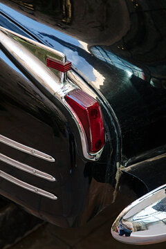 Detailed close-up of a vintage black car's red rear taillight and polished chrome trim