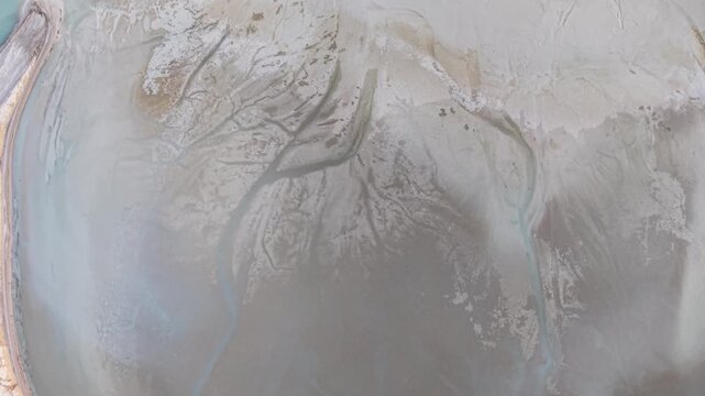 Top down drone footage captures branching dark channels etched through pale shallow sediment near the Lake Huron shoreline