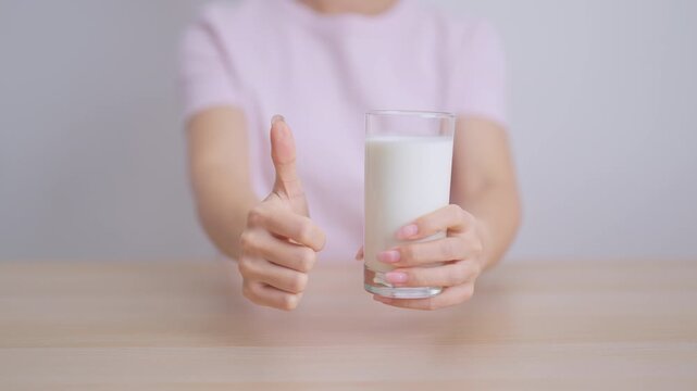 Healthy woman with glass of fresh milk and show thumbs up at home, female drinking for calcium and strong bones, high protein, dairy product for healthy lifestyle, wellness and daily routine concept