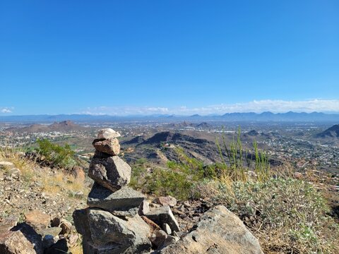 Rock cairn stack on a mountain summit overlooking the expansive desert valley and city landscape of Phoenix, Arizona