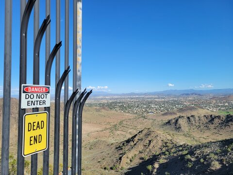North Mountain Park warning signs on a metal barrier looking down at the desert city landscape under a bright blue sky