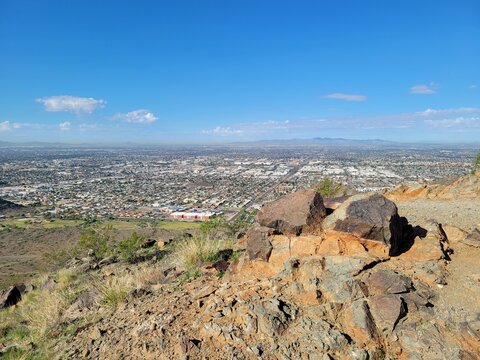 Rocky mountain edge overlooking an expansive panoramic cityscape and desert valley in Phoenix, Arizona, under blue skies