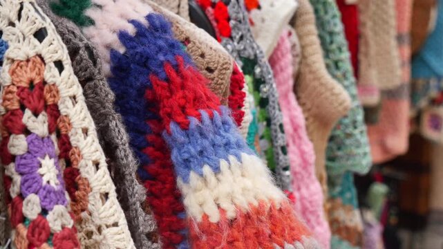 Hand-knit sweaters hang on display at a market stall during the day
