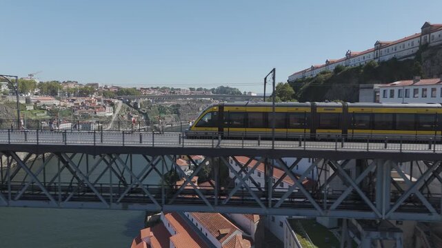 Yellow Metro do Porto train crossing the upper deck of the Dom Lu&iacute;s I iron bridge, with people walking beside the tracks above the Douro river.