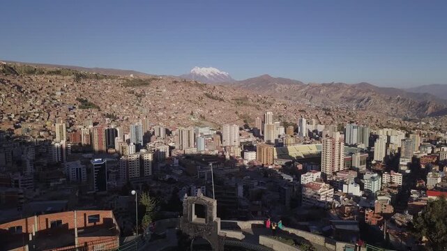 Drone flies forward over the stone arch of the Killi Killi viewpoint toward downtown La Paz and the snowcapped Illimani, Bolivia, Aerial