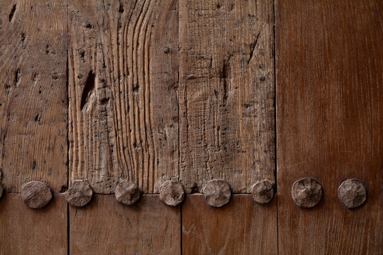 Close-up of weathered wooden surface with large nail heads and deeply textured grain