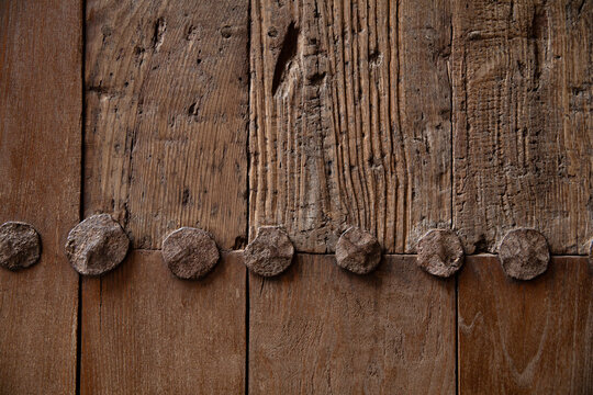 Close-up of weathered wooden surface with large nail heads and deeply textured grain