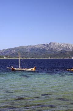 Lonely boat in clear blue water against a backdrop of mountains and clear sky, Bronn&ouml;ysund, Nordland, Rv 17, Kystriksveien, Norway