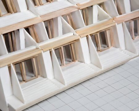 Detailed geometric facade model made from white styrene and basswood resting on printed grid paper brilliant natural daylight