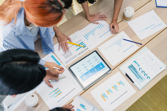 Overhead view of Asian business team reviewing PDCA plan do check act cycle on digital tablet with financial reports and revenue charts on office table