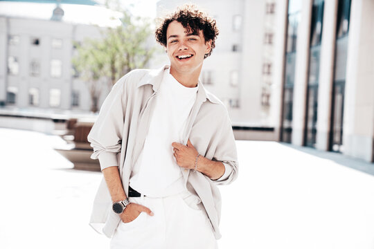 Portrait of young attractive man with curly hair hairstyle. Smiling handsome male in casual stylish clothes posing in the street at sunny day. Cheerful and happy model outdoors