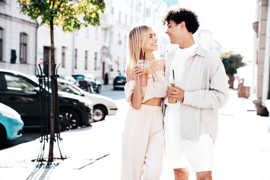 Young smiling beautiful woman and her handsome boyfriend in casual summer clothes. Happy cheerful family. Female having fun. Couple posing in street. Holding and drinking cocktail drink in plastic cup
