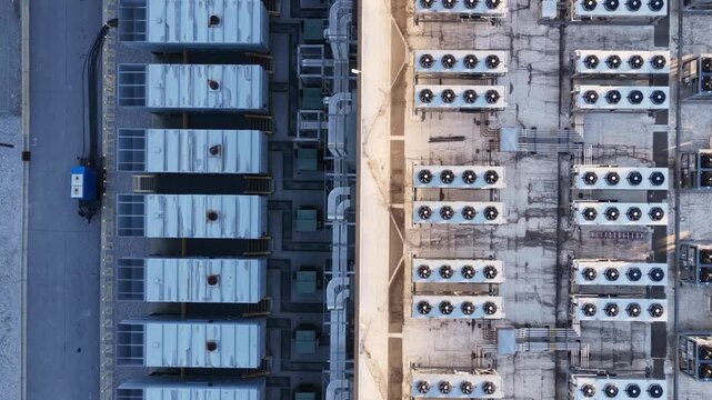Straight down over data center roof equipment, rows of condenser fans, air handling units and pipe racks catching low golden light and long shadows. Aerial top down