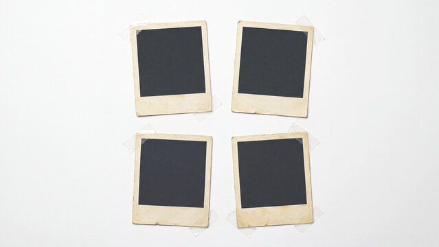 Four aged instant photo frames fixed with clear tape at the corners, yellowed blank vintage picture borders with dark empty window in a two by two grid, scrapbook and memory wall mockup on white