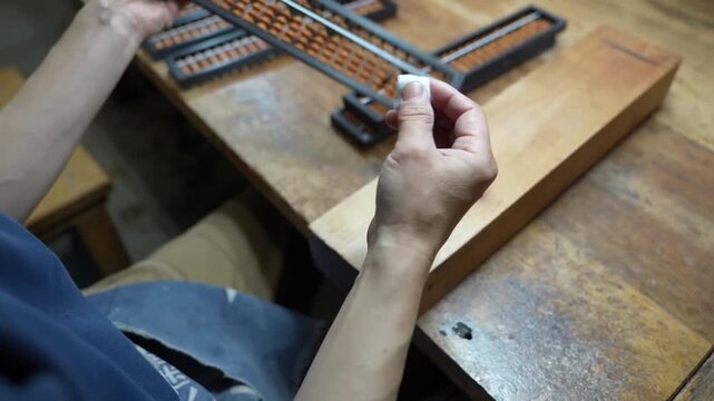 Craftsman inspecting row of finished wooden abacuses on old workbench