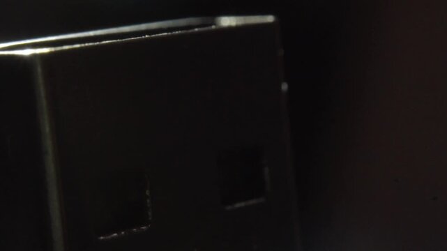 Panning shot of a black USB flash drive with a reflective metallic edge against a dark background, highlighting its compact design, smooth surface and electronic storage device form.