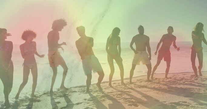 Eight adults dancing and posing on sandy beach near ocean horizon with bright colorful light flare
