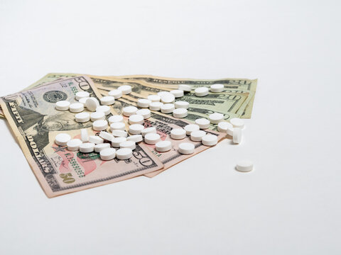 White Pills Scattered on US Dollar Bills Representing Healthcare Costs