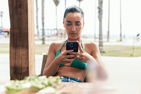 Concentrated woman wearing a bikini using her smartphone on a terrace near the beach