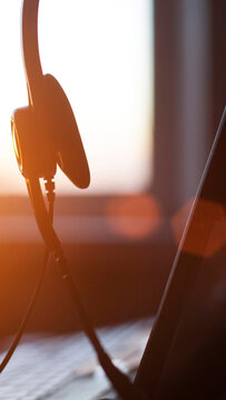 Headset with microphone close up illuminated by warm glow of sunset light on desktop computer keyboard in office or home setting, focused on communication technology detail, vertical photo