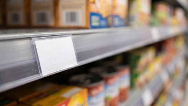 Empty blank price tag on supermarket shelf with blurred groceries