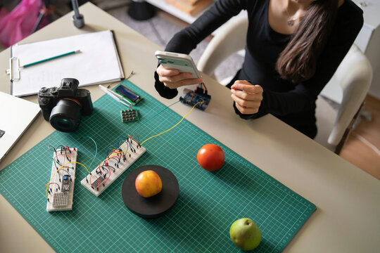 Top view of teacher creating online AI course about smart scales using microcontroller and smartphone.