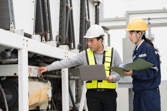Asian engineer and technician inspecting industrial cooling equipment, HVAC system and large air conditioning chiller units at rooftop of building