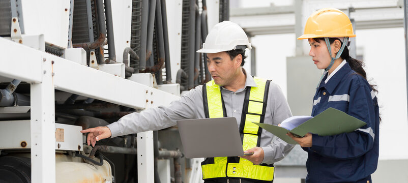 Asian engineer and technician inspecting industrial cooling equipment, HVAC system and large air conditioning chiller units at rooftop of building