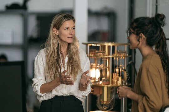 Two women having a professional conversation in a modern office with a gold structure in background