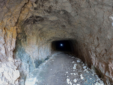 Wide angle view looking down a stone tunnel towards bright light at exit