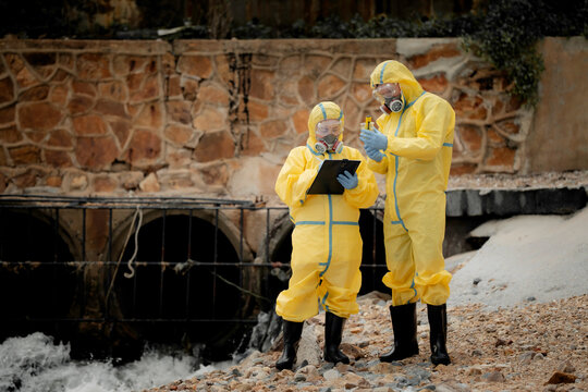 Hazardous chemical contamination inspection concept. Environmental scientists in protective suits collecting polluted water samples near industrial wastewater area. pollution, hazmat, safety,