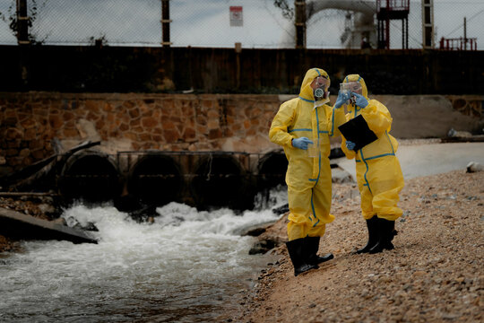 Hazardous chemical contamination inspection concept. Environmental scientists in protective suits collecting polluted water samples near industrial wastewater area. pollution, hazmat, safety,