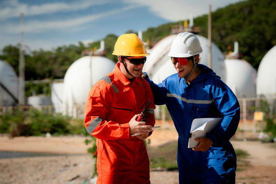 two professional engineer, worker, technician use clipboard discuss work, factory plant industry at a gas storage facility. protective uniforms and helmets. industry, engineer, safety, teamwork.