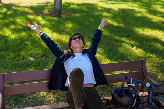 Hispanic woman sitting on bench stretching outdoors next to bicycle