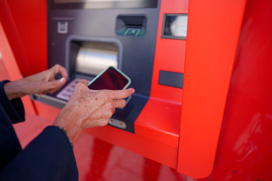 Hands using smartphone at red atm machine
