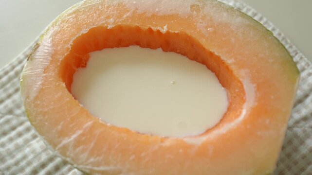 Pouring a milk mixture into a hollowed cantaloupe half