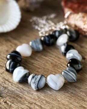 beautiful handmade bracelet made of carved heart shaped black and white agate stones resting on a rustic wooden surface for jewelry and fashion design illustration