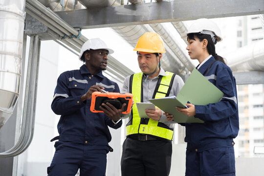 Team of multiethnic engineer and technician discussing maintenance check and safety operation at rooftop with large stainless steel HVAC ducts and pipe