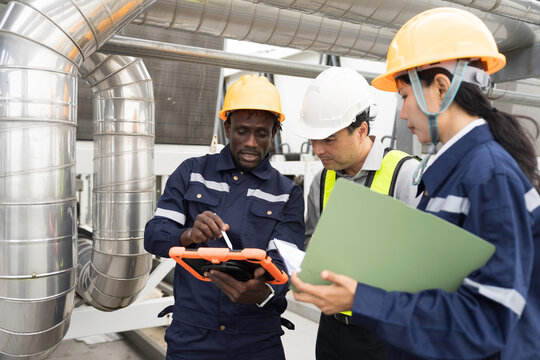 Professional engineer, technician team wearing hard hat and uniform inspecting industrial HVAC ventilation pipes and cooling system on rooftop using digital tablet and clipboard
