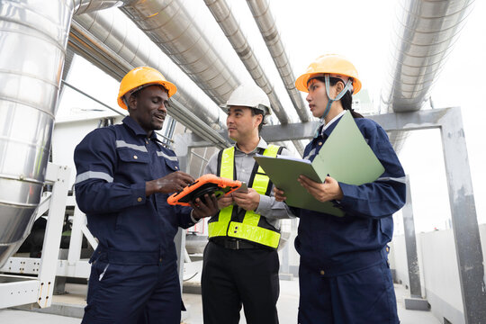 Professional engineer, technician team wearing hard hat and uniform inspecting industrial HVAC ventilation pipes and cooling system on rooftop using digital tablet and clipboard