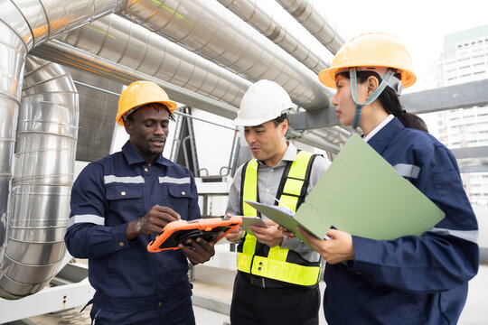 Professional engineer, technician team wearing hard hat and uniform inspecting industrial HVAC ventilation pipes and cooling system on rooftop using digital tablet and clipboard