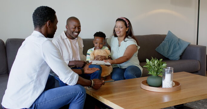 Diverse family enjoying quality time at home, reading book together on couch