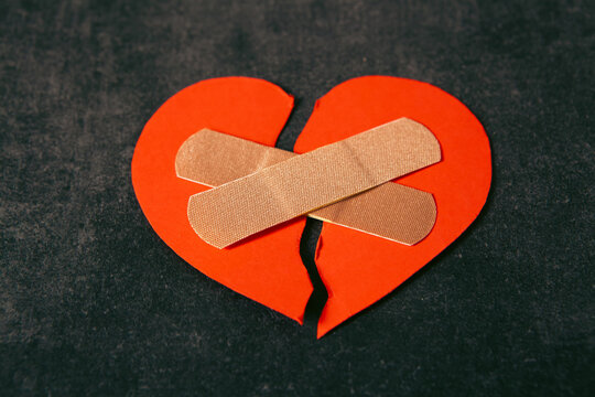 Broken heart with adhesive bandage on black background, closeup