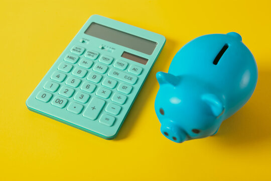 Blue piggy bank and calculator on yellow background. Saving money concept