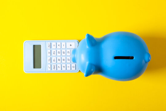 Blue piggy bank and calculator on yellow background. Saving money concept