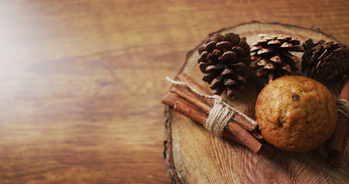 Image of christmas decorations with pine cones and cinnamon and cupcake on wooden background